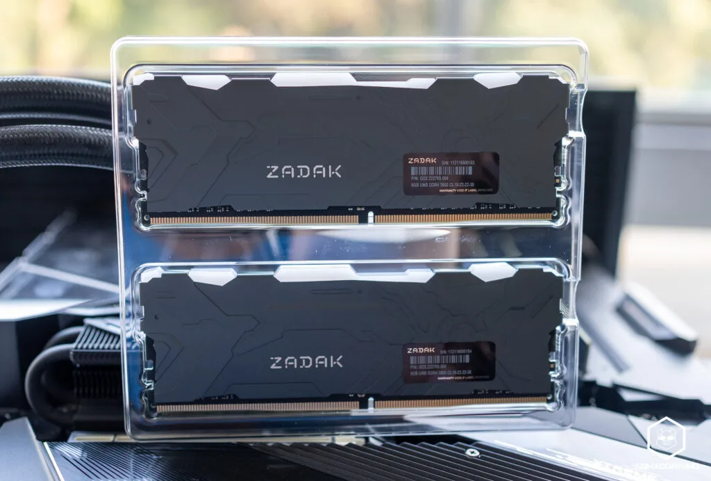 Módulos de RAM ZADAK en un soporte transparente, con un diseño negro y detalles en metal, sobre una superficie de computadora.