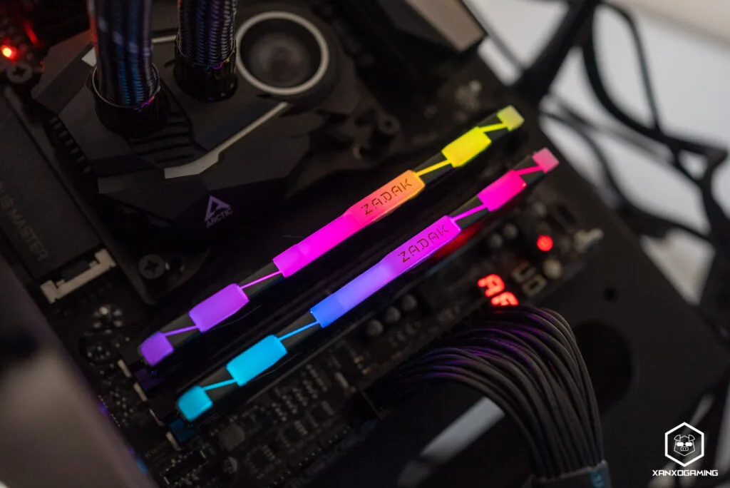 Memoria RAM con iluminación RGB en tonos púrpura, azul y amarillo, instalada en una placa base junto a un disipador de CPU oscuro.