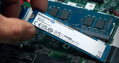 Disco SSD Kingston NV2 de 500GB en mano, instalado sobre una placa base con componentes electrónicos visibles en tonos azules y verdes.