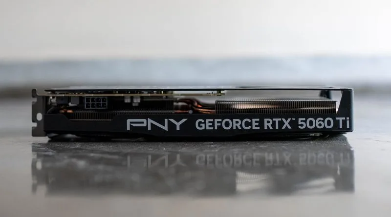 Tarjeta gráfica PNY GeForce RTX 5060 Ti, vista lateral, con un diseño en negro y detalles metálicos, sobre una superficie clara.