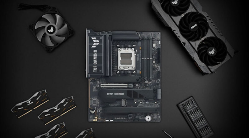 Placa base negra en el centro, rodeada de un ventilador, una tarjeta gráfica y varios componentes. Fondo oscuro.