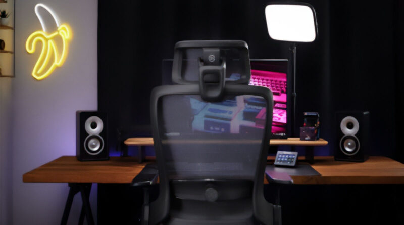 Silla ergonómica negra frente a un escritorio con monitores, altavoces y una lámpara. Fondo oscuro con un letrero de plátano iluminado.