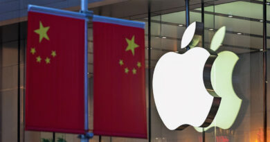 Banderas chinas rojas ondean junto al logo de Apple, iluminado y prominente, frente a un edificio moderno.