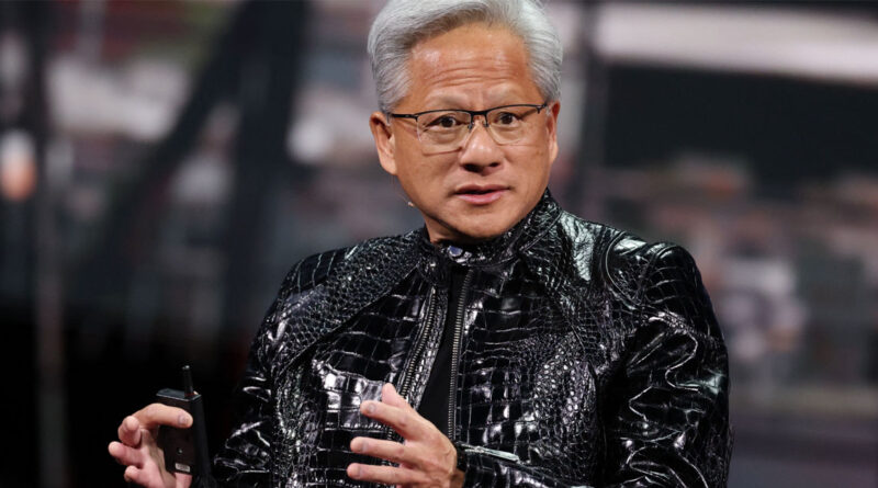 Jensen Huang, con cabello canoso y chaqueta negra brillante, habla en un escenario, sosteniendo un micrófono. Fondo difuso de evento tecnológico.