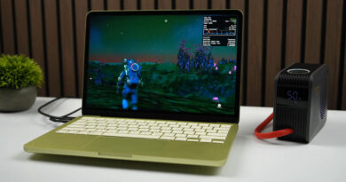 Laptop MacBook con pantalla de juego en un entorno alienígena, junto a un dispositivo de enfriamiento en una mesa blanca.
