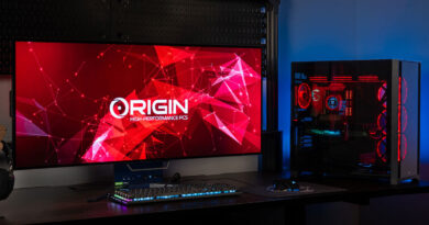 Pantalla grande con fondo rojo y gráfico geométrico, junto a una torre de PC iluminada en rojo y azul, con teclado y mouse RGB.