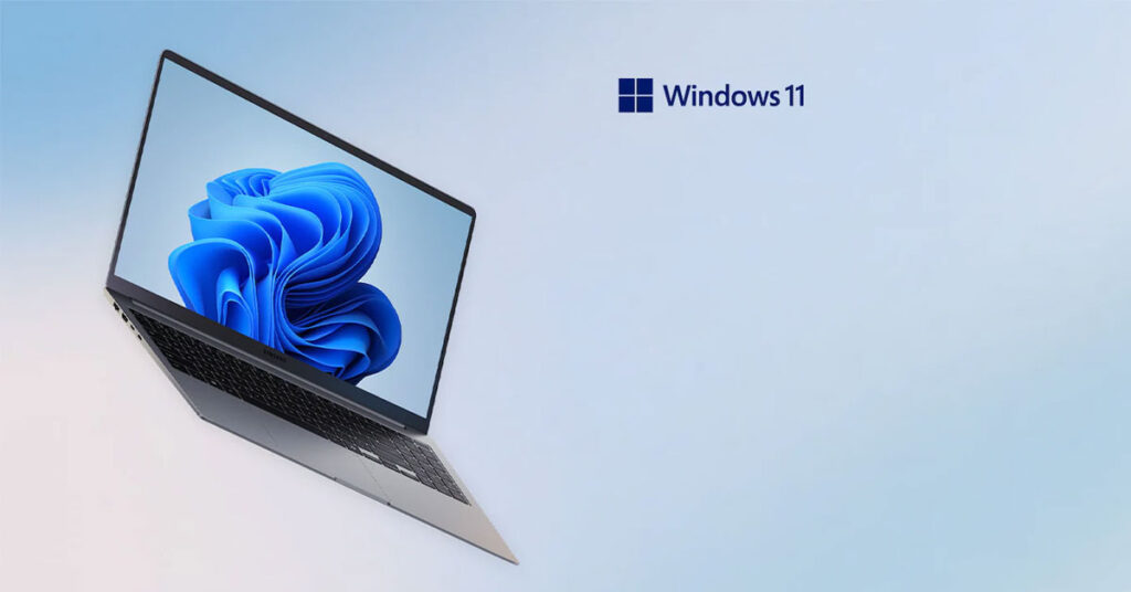 Portátil moderno con pantalla que muestra el logo de Windows 11, sobre un fondo suave en tonos azules.