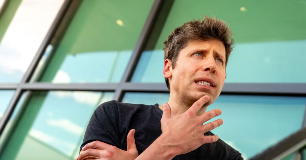 Hombre de cabello castaño claro con camiseta negra gesticula mientras habla, frente a un edificio con ventanas verdes.