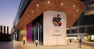 Fachada moderna de una tienda Apple, con luces brillantes y gráficos coloridos, mostrando un gran logo de Apple y un mensaje de "Próximamente".