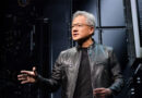 Jensen Huang, con chaqueta de cuero y gafas, habla en un escenario con fondo de circuitos y componentes tecnológicos.