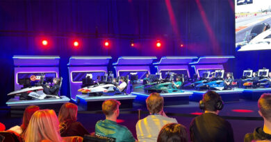 Seis simuladores de carreras con participantes compitiendo en un ambiente iluminado con luces rojas y azules, frente a una pantalla grande.