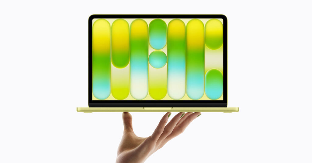 Un MacBook dorado sostenido por una mano, mostrando una pantalla con formas geométricas en tonos verdes y amarillos.