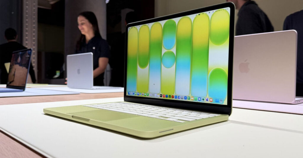 Laptop en color verde claro con pantalla brillante que muestra un fondo en tonos amarillos y verdes, colocada sobre una superficie clara.