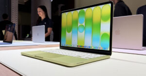 Laptop en color verde claro con pantalla brillante que muestra un fondo en tonos amarillos y verdes, colocada sobre una superficie clara.