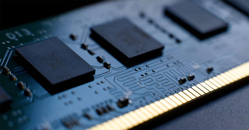 Módulo de memoria RAM con circuitos impresos, chips oscuros y contactos dorados, sobre un fondo oscuro y suave.