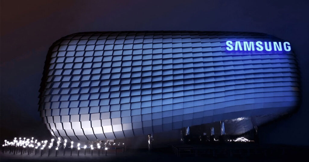 Edificio moderno de Samsung con fachada ondulada y letras brillantes, iluminado en tonos azules y con luces en el suelo.