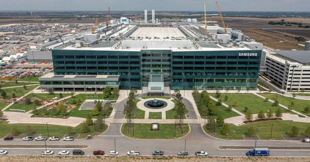 Fábrica de Samsung en Taylor, EE.UU., con un edificio moderno y amplio, árboles alineados y vehículos en el estacionamiento.