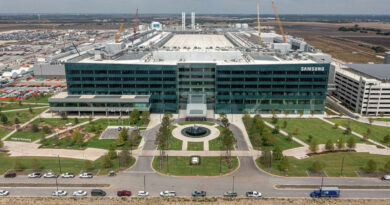 Fábrica de Samsung en Taylor, EE.UU., con un edificio moderno y amplio, árboles alineados y vehículos en el estacionamiento.