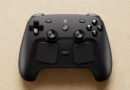 Controlador negro con dos joysticks, botones frontales y un diseño moderno, sobre un fondo claro y texturizado.