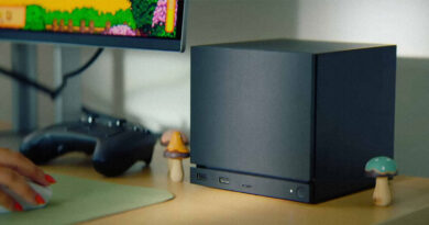 Computadora compacta negra sobre un escritorio, con un monitor que muestra un juego retro y decoraciones de hongos a los lados.