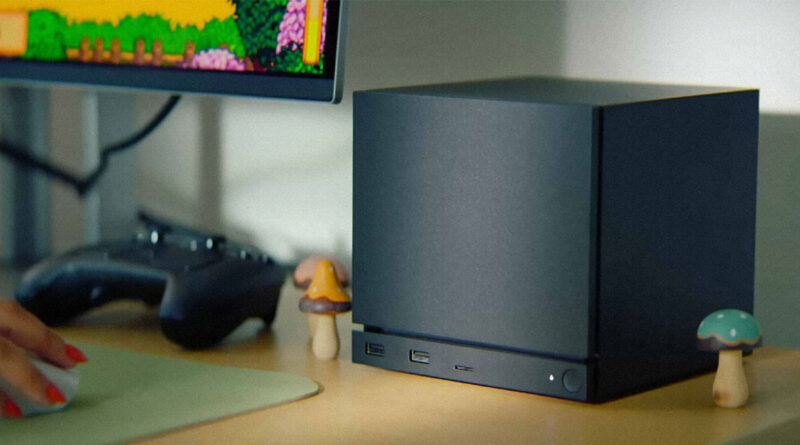 Computadora compacta negra sobre un escritorio, con un monitor que muestra un juego retro y decoraciones de hongos a los lados.