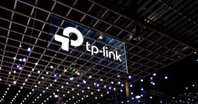 Logotipo de TP-Link suspendido en un espacio iluminado con luces colgantes, sobre un fondo oscuro de una feria tecnológica.