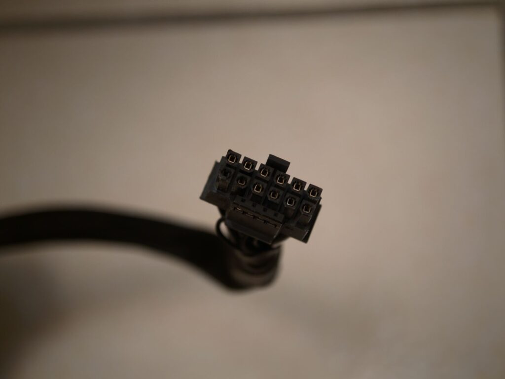 Conector de alimentación de una GPU, exhibiendo múltiples pines en un fondo neutro, con un enfoque en los detalles del conector.