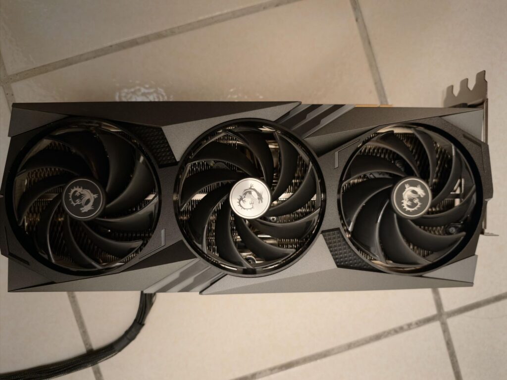 Tarjeta gráfica RTX 4090 con tres ventiladores negros, colocada sobre un suelo de cerámica clara.