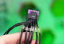 Conector de cable de alimentación ASUS ROG Equalizer, negro con terminaciones moradas y múltiples hilos, sostenido por una mano, fondo verde.