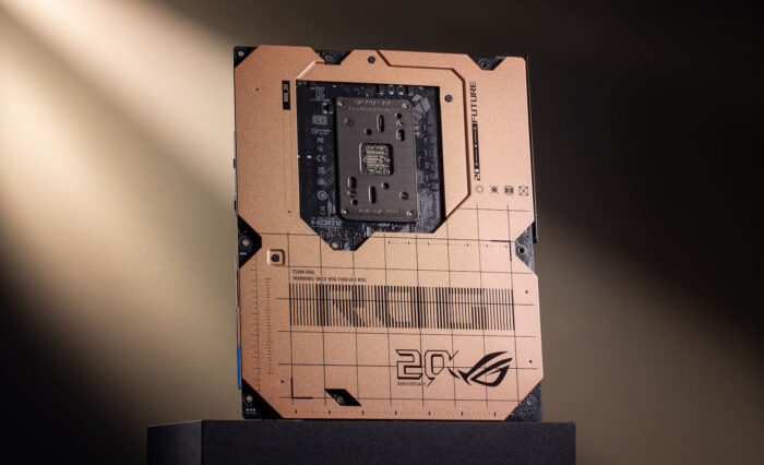 Placa base ROG Crosshair en color cobre, con detalles geométricos y el logo de 20 años, iluminada desde atrás sobre un fondo oscuro.