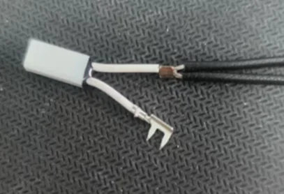 Conector 12V-2x6 con aislante blanco, cables expuestos y terminal tipo horquilla, sobre fondo texturizado negro.