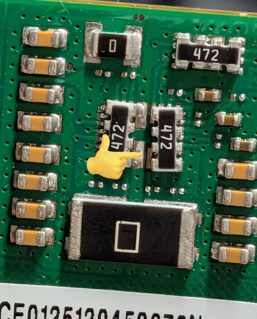 Placa de circuito con componentes electrónicos pequeños, etiquetas "472" en resistencias, fondo verde y conexiones metálicas.