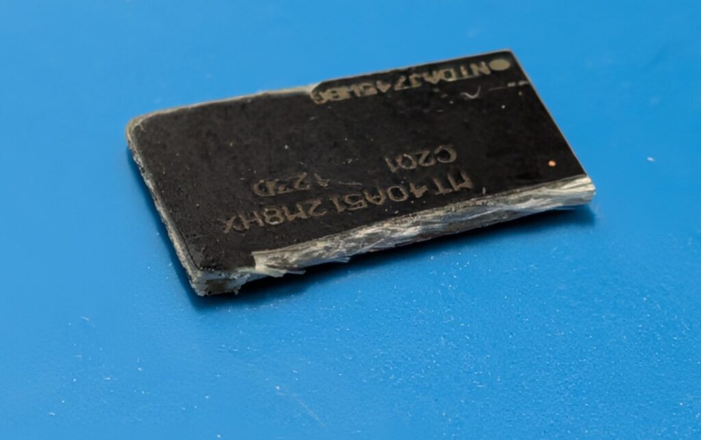 Chip de circuito negro sobre fondo azul, con texto en relieve que incluye números y letras; presenta signos de desgaste en los bordes.