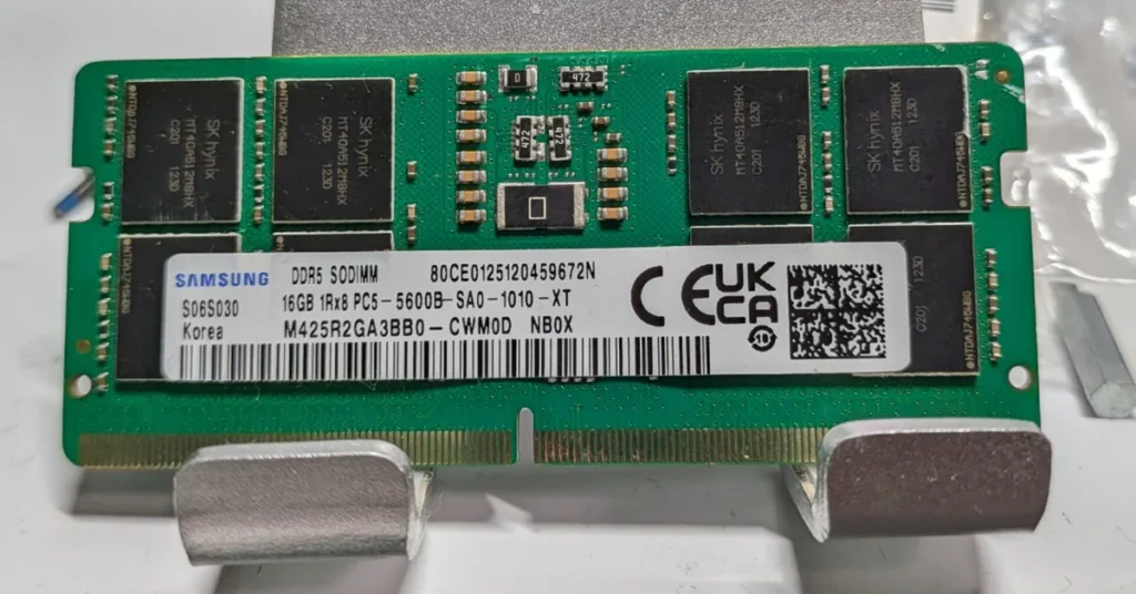 Módulo de memoria DDR5 SO-DIMM con chips de plástico, etiqueta blanca y verde, texto en negro, varios chips oscuros a lo largo.