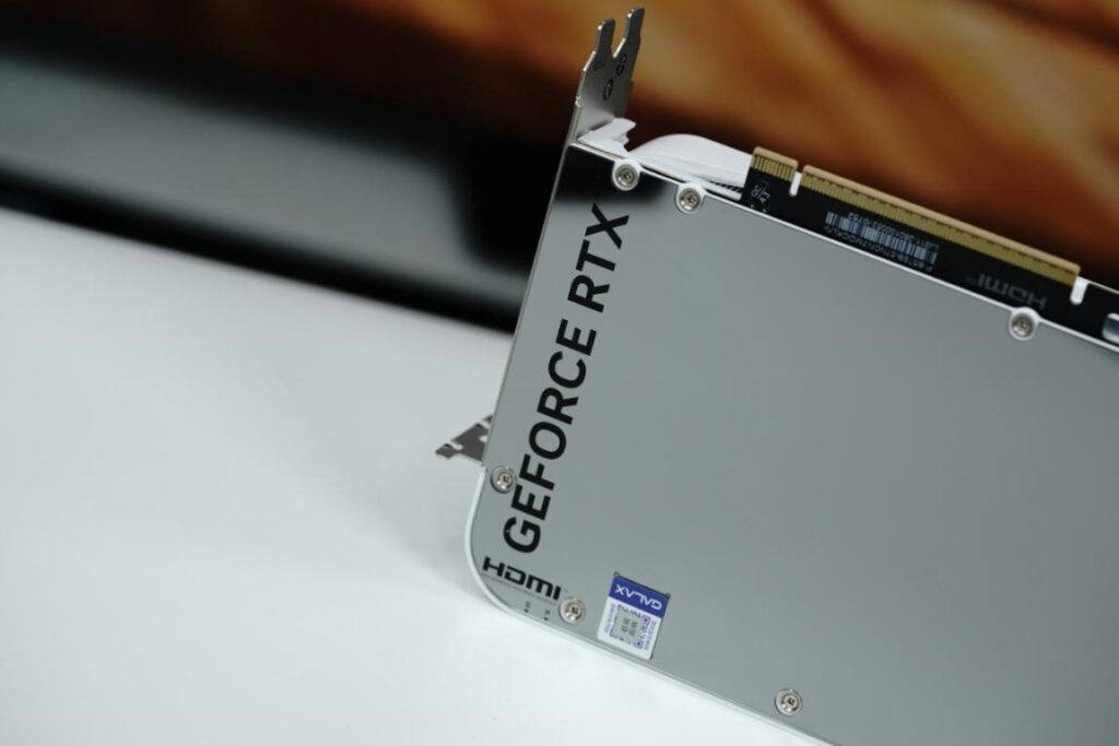 Tarjeta gráfica GeForce RTX con diseño plateado y logotipo prominente, conectores HDMI visibles y fondo desenfocado.