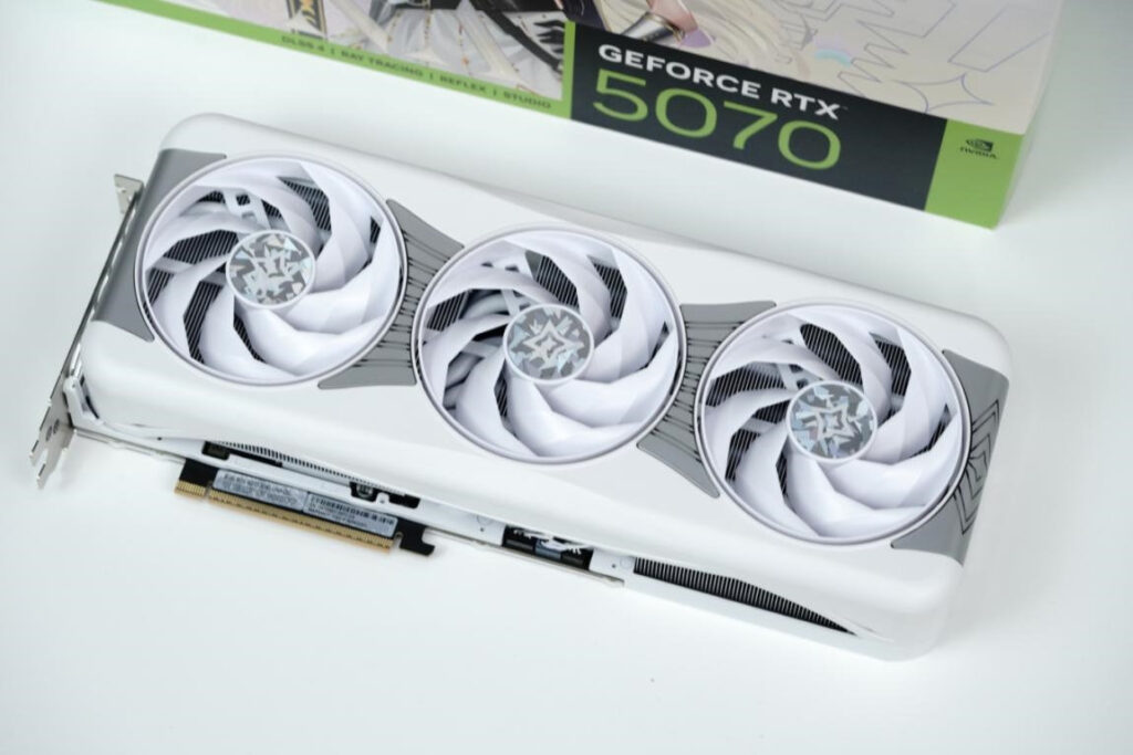 Tarjeta gráfica GeForce RTX 5070 con tres ventiladores en blanco y gris, diseñada con un estilo moderno y elegante.