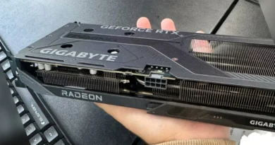 Tarjeta gráfica Gigabyte RTX 5060 Ti con disipador de Radeon, sostenida en una mano, en un fondo de mesa oscura.