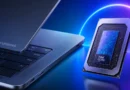 Portátil Googlebook con una tapa gris y teclado oscuro, junto a un procesador Intel Core brillante sobre fondo azul y púrpura.