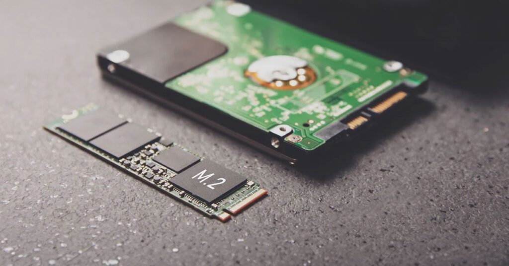 SSD M.2 en primer plano junto a un disco duro tradicional, sobre un fondo oscuro con detalles metálicos y circuitos.