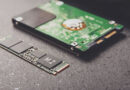 SSD M.2 en primer plano junto a un disco duro tradicional, sobre un fondo oscuro con detalles metálicos y circuitos.