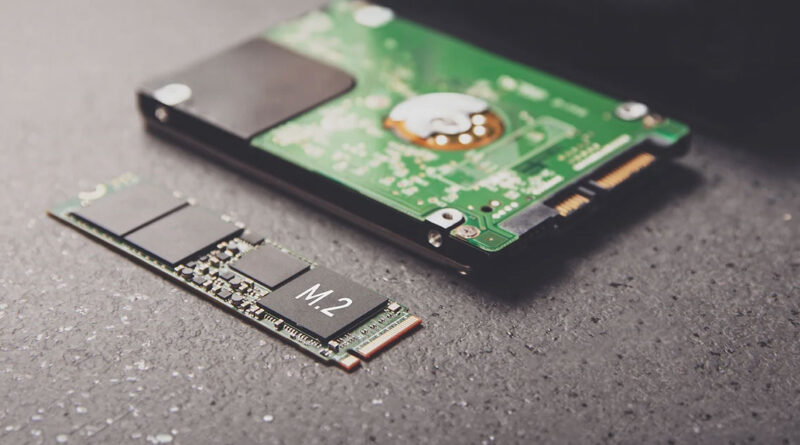 SSD M.2 en primer plano junto a un disco duro tradicional, sobre un fondo oscuro con detalles metálicos y circuitos.