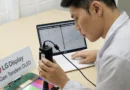 Un técnico examina un panel de LG Display con un dispositivo de medición, mientras que un portátil muestra datos en el fondo.