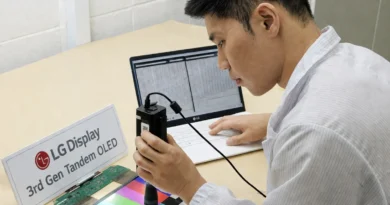 Un técnico examina un panel de LG Display con un dispositivo de medición, mientras que un portátil muestra datos en el fondo.