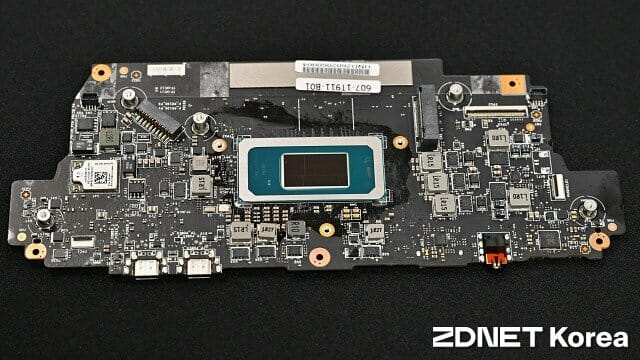 Placa de circuito impreso negra con un chip central en tonos plateados y azules, conectores y componentes electrónicos distribuidos.