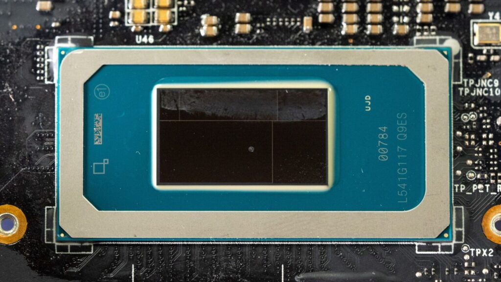 Chip de GPU en la placa base, con un marco plateado y un fondo negro. Se observa un diseño detallado y componentes electrónicos alrededor.