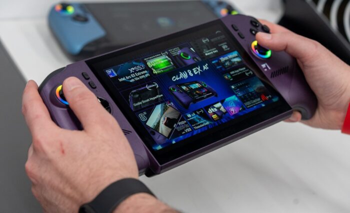 Controlador de consola portátil en manos de un usuario, con pantalla táctil que muestra varios juegos y un diseño moderno en tonos morados.