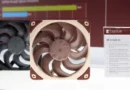 Ventiladores de computadora de Noctua: uno en tonos negro y otro en marrón claro con marco rojo. Detalle de características al lado.