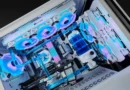Ensamblaje de PC gaming con refrigeración líquida, componentes en blanco y azul, y ventiladores LED iluminados en tonos azules y rosas.