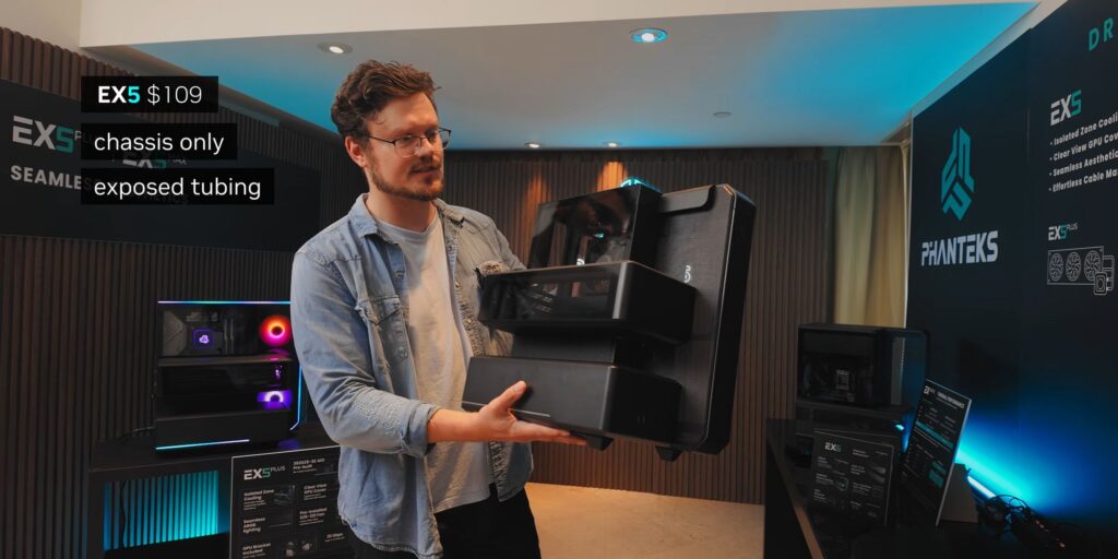 Hombre sosteniendo un chasis de PC negro de la serie EX5, con tubos expuestos, en un entorno de exhibición moderno.
