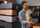 Un hombre sostiene una caja negra mientras se exhiben varias cajas de PC en colores gris, dorado y negro en un fondo moderno.